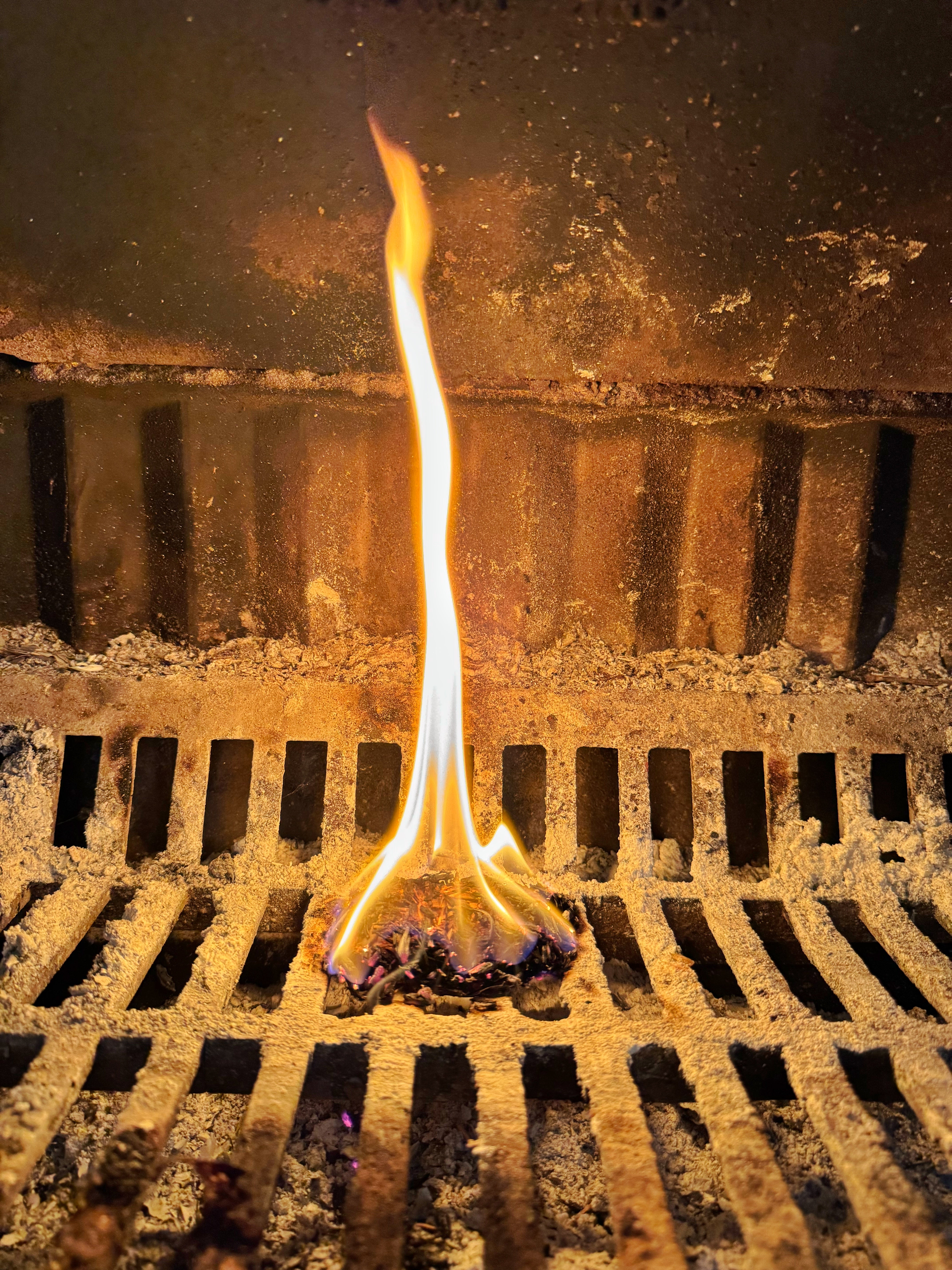 Woodcycle Firelighter Tea Bag burning on a metal grate with a dark background